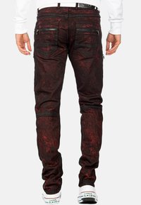 Jeans strappati neri e rossi con tasche con zip, a vestibilità slim e cuciture dettagliate, indossati con sneakers alte bianche.