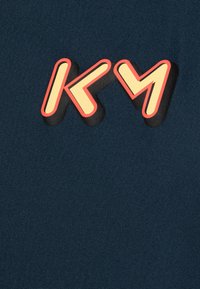 Tela azul navy con un gráfico en relieve en letras amarillas y rojas que dice "KY". El diseño tiene un estilo moderno y juguetón con colores en contraste audaces.