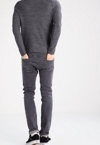 Gray knit long-sleeve shirt, fitted design. Paired with slim-fit dark gray jeans. Black sneakers with white accents complete the outfit.