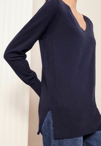 Granatowy sweter z dzianiny z dekoltem w kształcie litery V, długimi rękawami i rozcięciami po bokach u dołu, z teksturowanym wykończeniem i akcentami w prążki.