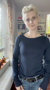 Jūros jėgos ilgomis rankovėmis marškiniai su plačiu iškirpimu, dėvimi su tamsiomis džinsomis ir juodu diržu su sidabriniais akcentais. Vidinė aplinka su knygomis fone.