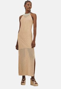 Vestido largo de punto en beige con un patr�ón de diamantes, escote halter, aberturas laterales y complementado con un collar de múltiples hilos. Lleva unas cuñas de plataforma.