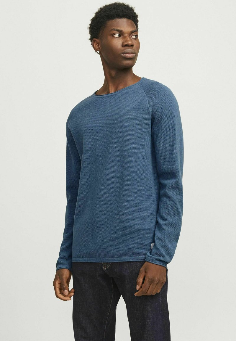 Blå tekstureret langærmet skjorte med rund halsudskæring og raglanærmer, parret med mørke denimjeans. Subtile syninger ved manchetterne.