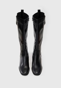 Botas de cuero negras hasta la rodilla con cremallera lateral y detalle de hebilla, punteras cuadradas y lengüetas en la parte superior, mostradas de frente.