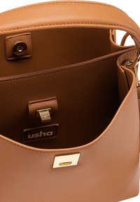 Indvendig brun taske i syntetisk læder med en glat tekstur, gyldent metal, lukning med spænde og diskret mærkning på en brun label.