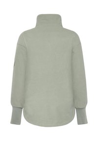 Jasnozielony polar z wysokim kołnierzem, długimi rękawami i zaokrąglonym dołem. Miękka faktura, bez widocznych wzorów czy elementów metalowych.