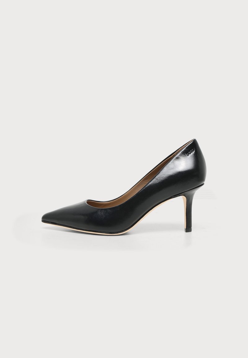 Chaussure à talon haut en cuir noir à bout pointu avec un talon kitten fin et une finition lisse et brillante sur fond blanc.