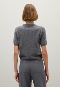 Suéter gris de manga corta en punto suave con escote redondeado y dobladillo acanalado, combinado con pantalones grises de corte ajustado, visto desde la parte posterior.