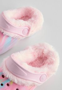 Chaussons roses en peluche, dotés d'un intérieur en matière douce, d'une large sangle et de trous de ventilation. L'extérieur présente un motif dégradé coloré.