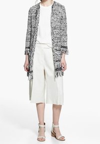 Szary i biały pleciony kardigan z frędzlami, noszony na białej koszulce i jasnobeżowych szortach w szerokim kroju. Uzupełniony jasnymi sandałami.