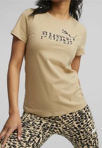 Beige short-sleeve t-shirt featuring a black and beige leopard print "PUMA" logo. Worn with patterned black and beige leggings.