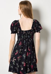 Mustat kukkakuosiset mekko puff-hihalla, rypytetty yläosa ja syvä V-muoto selässä. Sisältää värikkäitä kasvitulosteita ja lainehtivan helman.