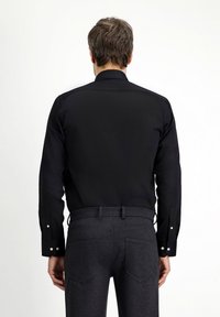 Czarna koszula z usztywnianym kołnierzykiem, długimi rękawami i guzikami na mankietach. Nosi się ją z ciemnoszarymi spodniami, o dopasowanym kroju i kieszeniach.