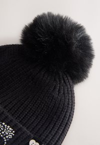 Gorro de invierno tejido negro con un gran pompón esponjoso en la parte superior y una pequeña sección de detalles con brillantes en el puño.
