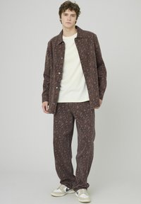 Ensemble veste et pantalon marron à motifs en tissu doux, présentant un motif de feuilles. Associé à un t-shirt de couleur claire et des baskets.