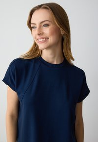 Top azzurro scuro a maniche corte realizzato in tessuto morbido, con scollatura rotonda e maniche raglan, caratterizzato da una texture liscia e una vestibilità casual.