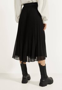 Gonna midi plissettata nera realizzata in materiale leggero, con una vita aderente e una texture fluida. Abbinata a stivali neri chunky.