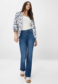 Witte top met een ronde hals, bloemenpatroon blouse in blauw en wit, blauwe flare jeans en witte sandalen met een tan kleurige zool.