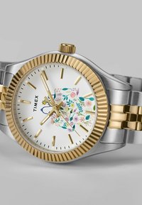 Silver and gold stainless steel watch with a floral-patterned white dial, gold hour markers, and a ridged bezel. Adjustable bracelet strap.