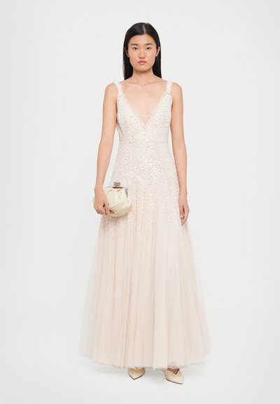 Mouwloze roze jurk met een diepe V-hals, versierd met pailletten en tule lagen, gecombineerd met een crèmekleurige clutch en nude hakken.