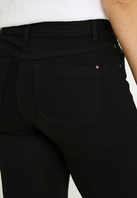 Jeans de mezclilla negra con un diseño ajustado, bolsillos traseros estándar y un sutil detalle de costuras a lo largo de la cintura y los bolsillos.