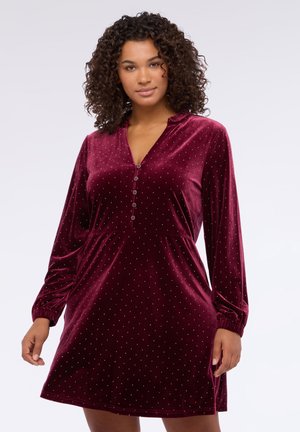 Bordowa aksamitna sukienka z długimi rękawami, z kołnierzykiem i zapięciem na guziki, ozdobiona małymi srebrnymi kropkami jako detalami akcentującymi.