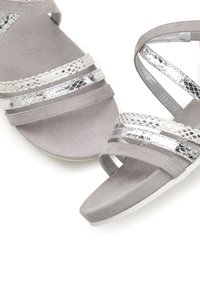 Grijze suede sandalen met zilveren metalen banden met een slangpatroon en een kruisbandontwerp. Platte zool met tekstuurdetails.