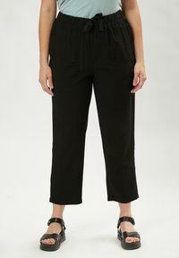 Pantaloni neri, comodi e larghi, con vita elastica e cordoncino. Il tessuto ha una consistenza liscia e gambe corte. Abbinati a sandali neri.