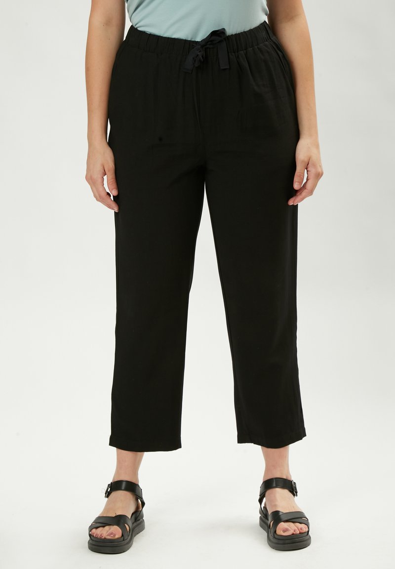 Pantaloni neri, comodi e larghi, con vita elastica e cordoncino. Il tessuto ha una consistenza liscia e gambe corte. Abbinati a sandali neri.