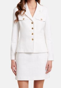 Bílý strukturovaný blazer se zlatými knoflíky a dvěma náprsními kapsami, v kombinaci se slušivou bílou sukní se vypasovaným střihem.