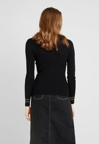 Haut noir à manches longues côtelé, au design ajusté, avec des accents clairs aux poignets. Associé à une jupe en denim foncé avec poches.