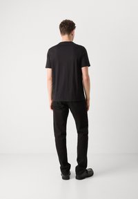 Sort kortærmet T-shirt med lige snit, lavet af blødt stof, parret med sorte jeans og sorte sko. Enkel design, uden synlige logoer.