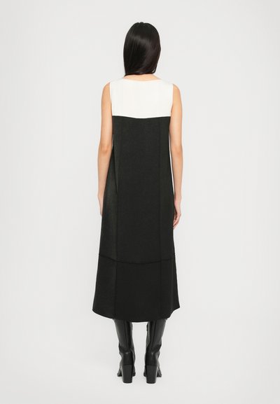 Mustvalge ilma varrukateta kleit, millel on struktureeritud disain, tekstureeritud kangas ja põlvepikkune ääres, kantud mustade põlvikute saapastega.