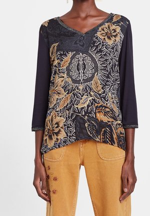 Top negro de manga larga con estampado floral beige y marrón, combinado con pantalones color mostaza que presentan pequeñas flores bordadas.