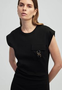 Czarny bezrękawnik z miękkiego materiału, z kieszenią na przodzie i złotymi oraz niebieskimi akcentami, oraz okrągłym dekoltem.