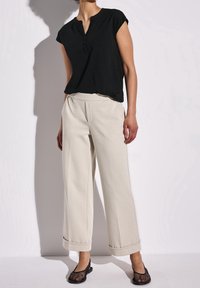 Černý krátký rukávový top s knoflíkovým výstřihem, v kombinaci se smetanovými kalhotami širokého střihu s ohrnutými manžetami a jemnými záhyby, obutý s černými balerínami.