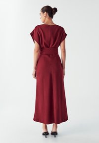 Bordo haljina s kratkim, drapiranim rukavima, strukom na vezanje i dugom, lepršavom suknjom. Glatka tkanina s suptilnim sjajem.