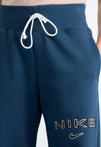 Närbild av marinblå Nike sweatpants med vit dragsko och broderad Nike-logotyp på vänster lår.
