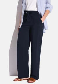 Navyblauwe, wijde broek met een elastische tailleband en een trekkoord, gemaakt van lichtgewicht stof. G gedragen met een witte blouse en bruine sandalen.