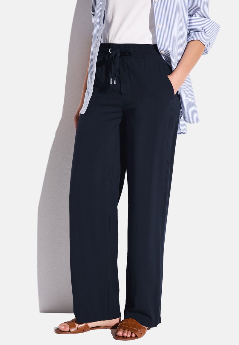 Navyblauwe, wijde broek met een elastische tailleband en een trekkoord, gemaakt van lichtgewicht stof. G gedragen met een witte blouse en bruine sandalen.