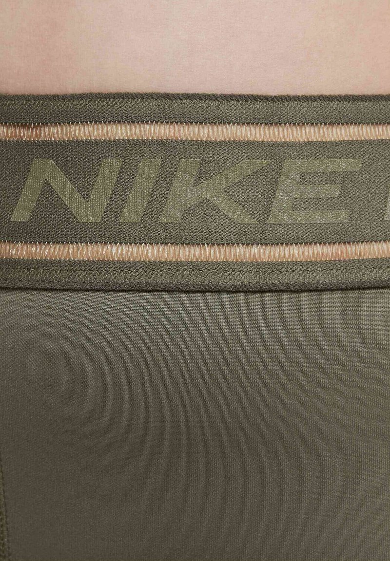 La cintura atletica verde oliva presenta una fascia spessa con dettagli cuciti e il logo "NIKE" in rilievo di una tonalità più chiara, mostrando una texture di tessuto liscia.