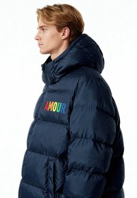 Veste matelassée bleu marine avec un col montant, ornée de lettres multicolores "AMOUR" sur le côté gauche de la poitrine, fabriquée en tissu lisse et brillant.