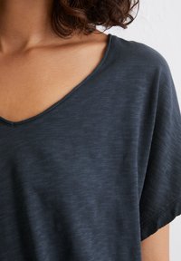 T-shirt grigio scuro a V in morbido tessuto leggermente testurizzato. Presenta maniche corte e una vestibilità rilassata con una leggera fantasia.