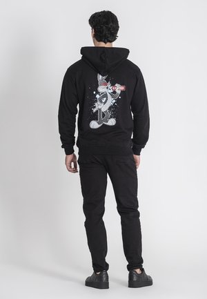 Zwarte hoodie met een cartoonfiguur graphic en tekst op de achterkant, gemaakt van zachte stof. Gepaard met zwarte jeans en sneakers.
