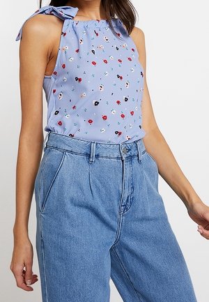 Vaaleansininen olkaimeton toppi, jossa on kukkakuosi, sidottavat hihnat ja rypytetty pääntie, yhdistettynä korkeavyötäröisiin vaaleansinisiin farkkuihin.