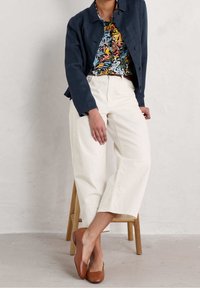 Veste marine, chemise à fleurs et pantalon blanc à larges jambes avec une coupe décontractée. Chaussures plates marron. Design simple et texture de matériau douce.