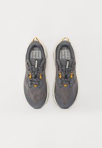 Chaussures de sport grises avec un dessus en mesh, accents jaunes, lacets réfléchissants et semelle amortie. Légères et conçues pour une utilisation en extérieur.