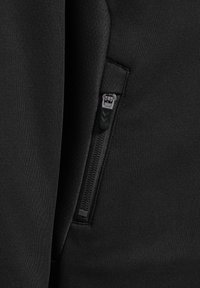 Svart idrottsjacka med texturerad tyg, en sned dragkedjeficka och ett mjukt, stretcht material för komfort och rörlighet.