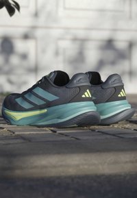 Sport shoes in dark blue with green accents, featuring a textured upper, three stripes design, and a textured sole for grip.