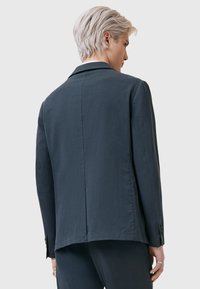 Mörkgrå blazer i ett mjukt tyg, med snedskuren krage, en slits och knappar vid ärmarna. Ren, minimalistisk design.